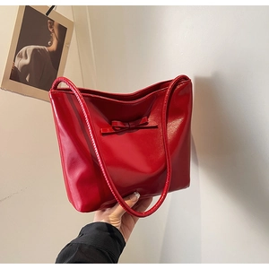Close-up of bright red glossy leather handbag with a delicate bow and slim strap