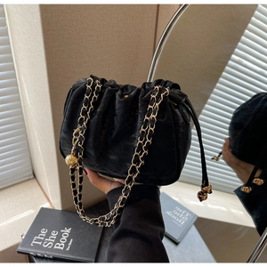 Detail view of a black velvet drawstring bag with gold metal chain and decorative gold ball