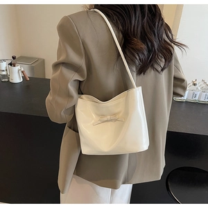 Detail of a creamy white leather tote bag with a bow decoration on a model's shoulder