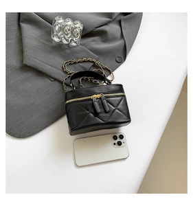 Detailed top view of black quilted diamond crossbody bag with gold chain next to phone