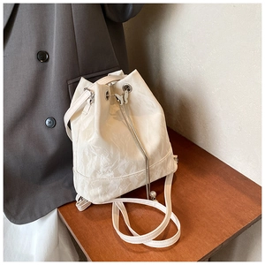 Detail of white drawstring bucket bag with silver butterfly charm and textured PU leather