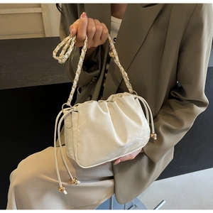 Detail of cream pleated cloud bag featuring gold drawstring accents and chain strap