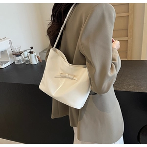 Chic white shoulder bag with bow detail worn by a model in a minimalist cafe setting