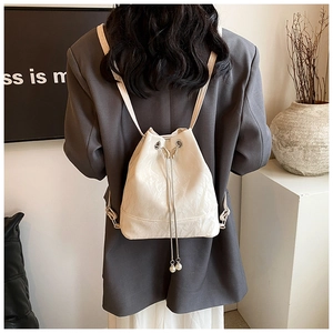 Detail of cream bucket backpack featuring butterfly buckle and pearl drawstring charms