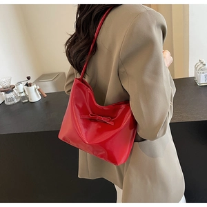 Close-up of a red patent leather shoulder bag featuring a decorative bow and sleek finish