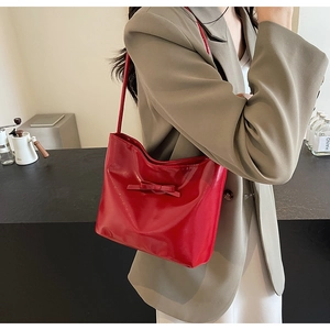 Macro shot of a red patent leather shoulder bag featuring a stylish bow detail and glossy finish