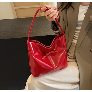 Detail of glossy red patent leather tote bag with bow detail held by a model