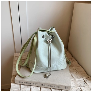 Detail of mint green bucket bag featuring a butterfly metal buckle and pearl drawstring