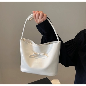 Detail view of a white glossy bucket bag featuring a large bow and top handle