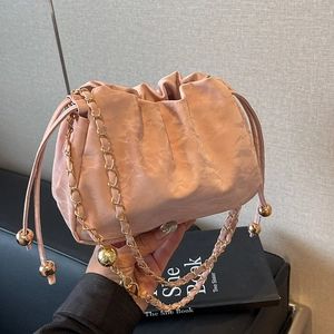 Chic pink drawstring cloud bucket bag with gold chain strap held by a model