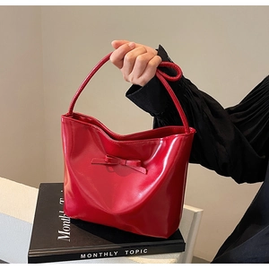 Detail of red glossy patent leather handbag featuring an elegant bow and single handle