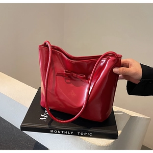 Detail of red glossy patent leather tote bag featuring a decorative bow on the front