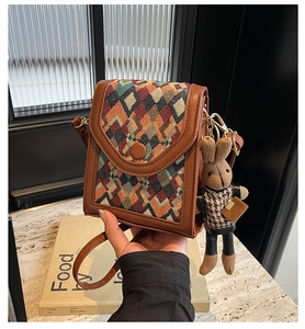 Detail of bohemian plaid phone bag with leather trim and cute rabbit doll keychain
