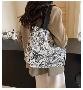 Detail of floral canvas tote bag with black wide strap shown over the shoulder