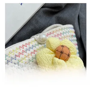 Detail of woven bag with colorful zigzag stitching, a floral accent, and pearl button closure