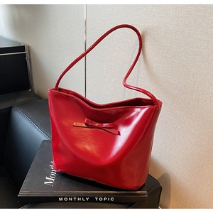 Detail of red shoulder tote bag with leather bow accent on a stack of books