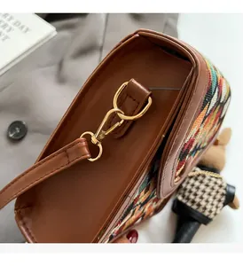 Close-up of golden metal hooks and stitched brown leather on a checkered crossbody bag