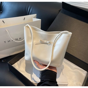 Close-up of a white leather tote bag with a bow knot design and slender handles