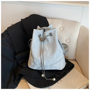 Detail of drawstring bucket bag featuring butterfly metal charm and silver snake chain