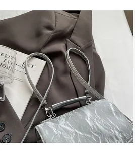 Detail of silver metallic textured crossbody bag with bow accents on a brown blazer background