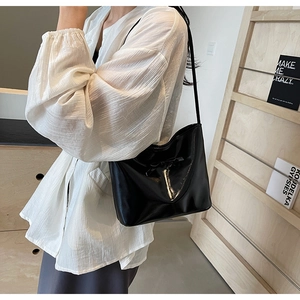 Glossy black underarm bag with bow detail worn over a white puff sleeve shirt