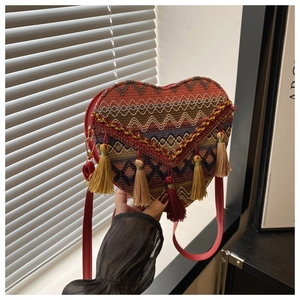Close-up of heart-shaped woven bag featuring colorful tassels and red shoulder strap