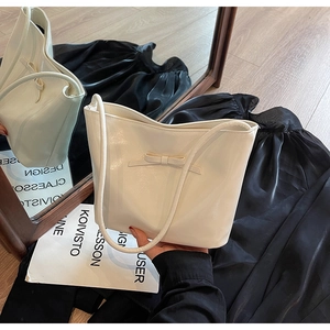 Detailed view of a white leather tote bag with a minimalist bow and slim shoulder strap