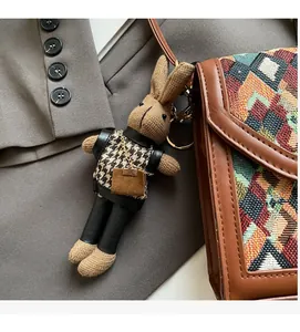 Detail of a brown handmade knit rabbit keychain with houndstooth outfit on a bag