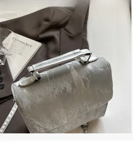 Silver marble pattern handbag with wide strap shown beside a brown suit and art card