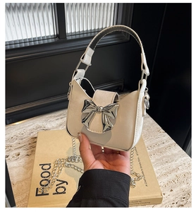 Detail of cream mini handbag with silver bow accent and metallic chain strap