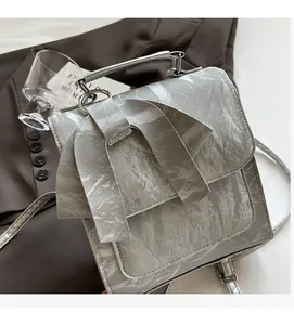 Detail of silver crossbody bag with large bow and metallic handle on textured leather