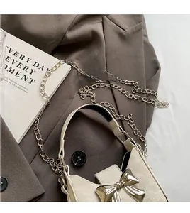 Close-up of cream mini bag with silver bow ornament and metallic chain strap detail
