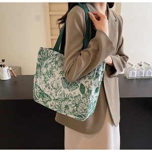 Detail of a large canvas tote bag with green butterfly print held by a model in a cafe