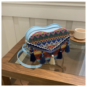 Detail of blue heart-shaped woven bag with bohemian embroidery and decorative tassels