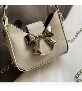 Close-up of mini cream crossbody bag featuring a large silver metal bow buckle detail
