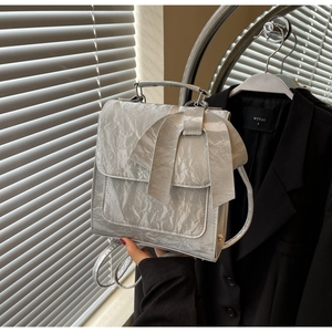 Detail of metallic silver crossbody bag featuring a large bow and crinkled texture fabric