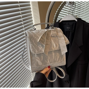 Detail of silver bow shoulder bag featuring metallic crinkled texture and round metal handle