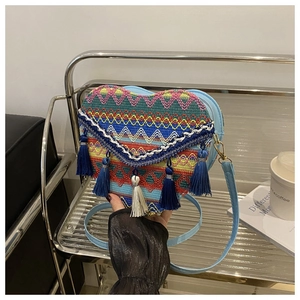 Detail of heart-shaped woven crossbody bag featuring colorful ethnic patterns and blue tassels