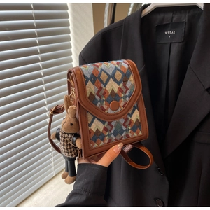 Detailed macro view of woven plaid crossbody bag featuring a brown plush rabbit charm
