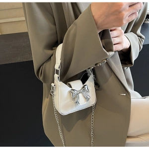 Detailed view of mini white leather crossbody bag with silver bow and metal chain strap