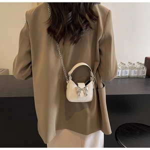 Close-up of mini cream crossbody bag with silver bow accent and chain strap on model