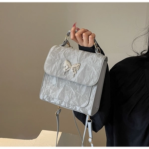Détail d'un sac argenté avec texture froissée et ornement papillon en métal chic