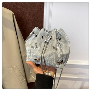 Detail of silver pleated bucket bag featuring metal butterfly and pearl drawstring
