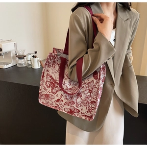 Detail of knit tote bag with floral patterns and red woven straps in a coffee shop setting