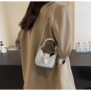 Mini silver bow crossbody bag shown on a model wearing a khaki oversized blazer jacket