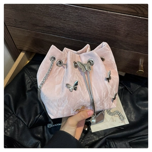 Detailed view of pink velvet bucket bag with silver butterfly charms and pearl strap