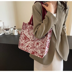 Detail of knit tote bag with red butterfly patterns worn with a beige blazer