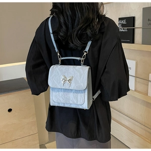 Détail du sac à dos bleu clair à texture froissée avec fermoir papillon argenté et lanières