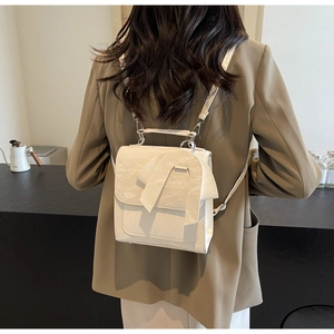 Detail of a chic cream-white backpack featuring a large bow and textured leather finish