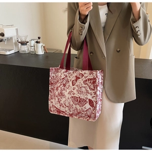 Detail of red butterfly and floral patterns on an off-white canvas tote bag with red straps